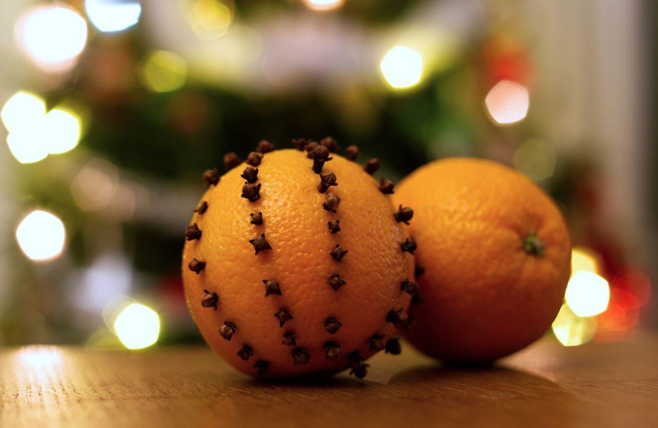 Pöydällä on kaksi appelsiinia, joista toiseen on pistelty mausteneilikoita.